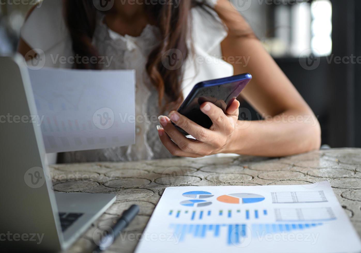 Female executives use mobile phones and are checking data graphs. Laptop, graphs and pen place on the desk. photo