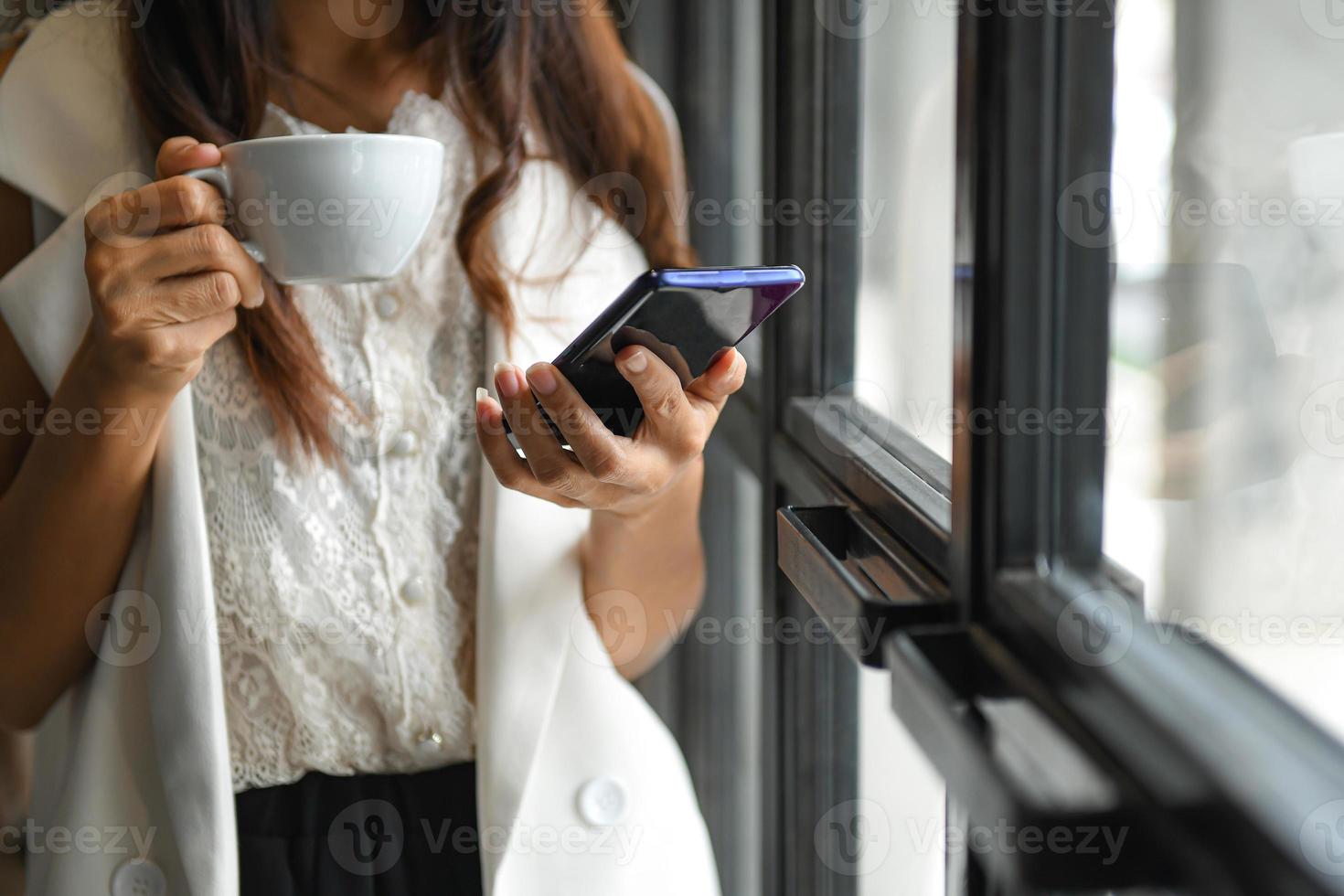 Female executive drink coffee and use smartphone during break.She stood by the window in the office. photo