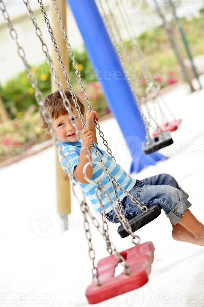 Little cute boy having fun on chain swings. photo