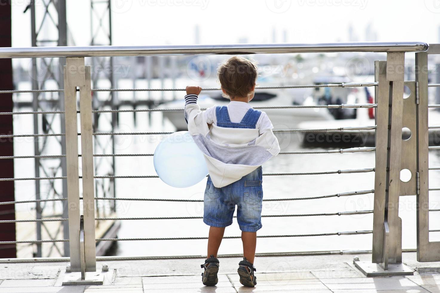 Small boy watching curiously yachts from behind the fence with ballun photo