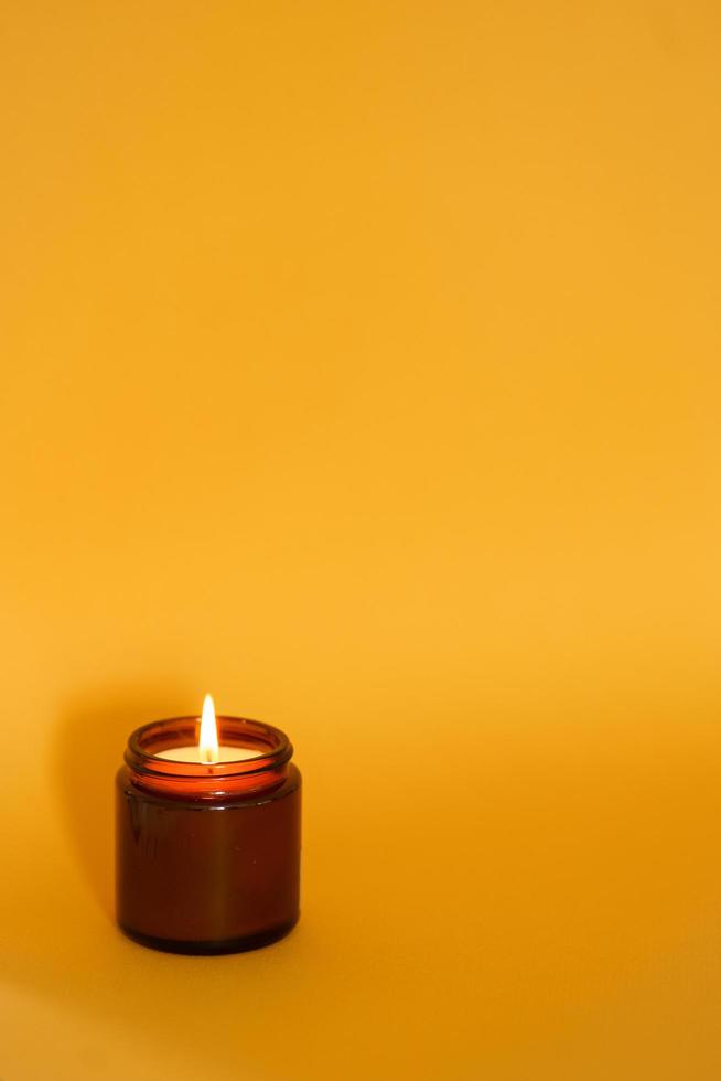 La quema de velas de soja en un frasco de vidrio oscuro se quema sobre un fondo amarillo. espacio libre para inscripción. calma y relajación foto