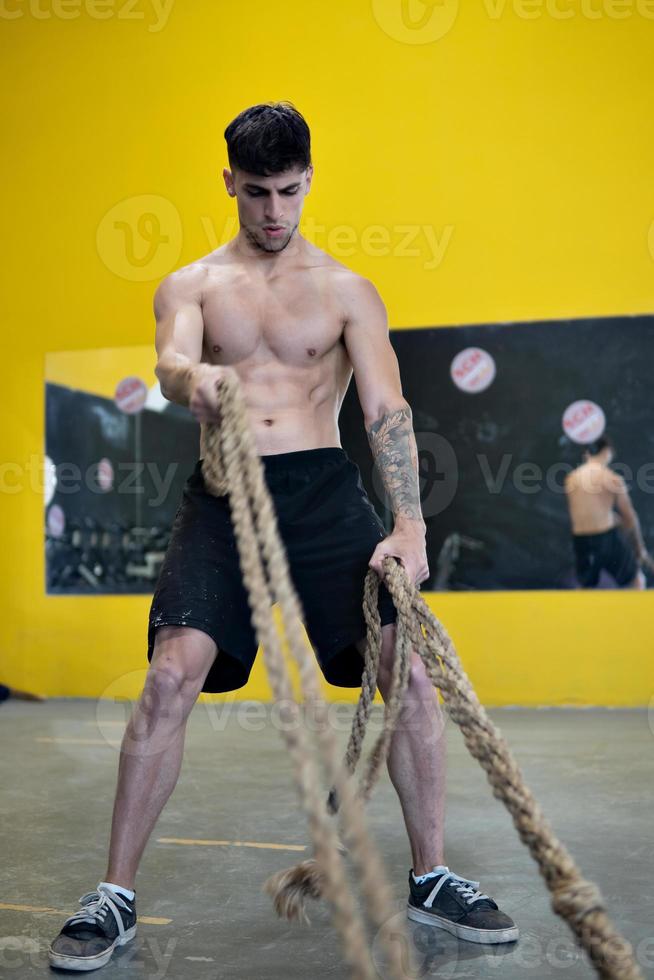 Fit man working out with battle ropes at fitness gym photo