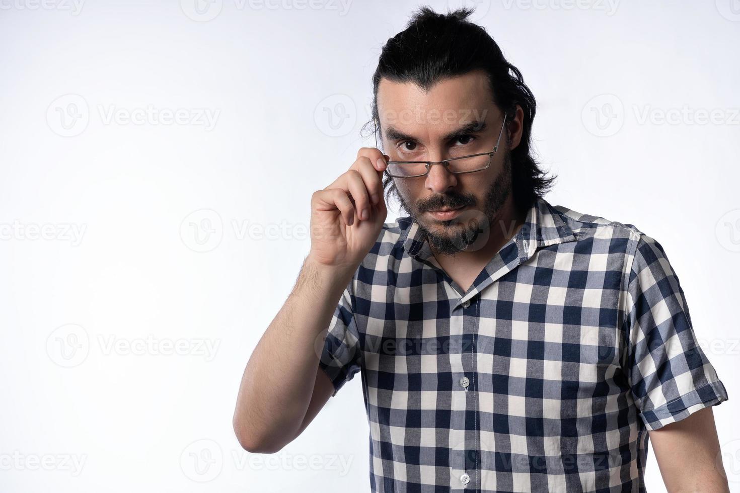 Close-up of lone man, with beard and glasses, looking at camera holding glasses to look over them. photo