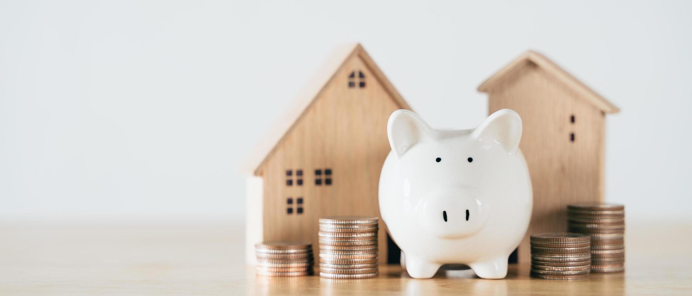 Wooden house with white piggy bank and stacking coins on wooden table. saving money for buying house, financial plan home loan concept. photo