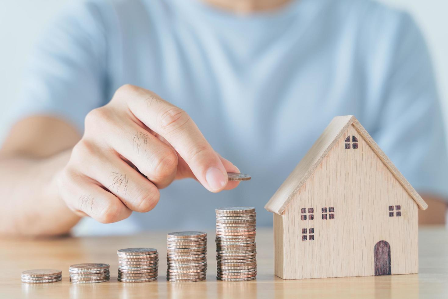 Man hand put coin on coins stack with wooden house on wood table. saving money for buying house, financial plan home loan concept. photo