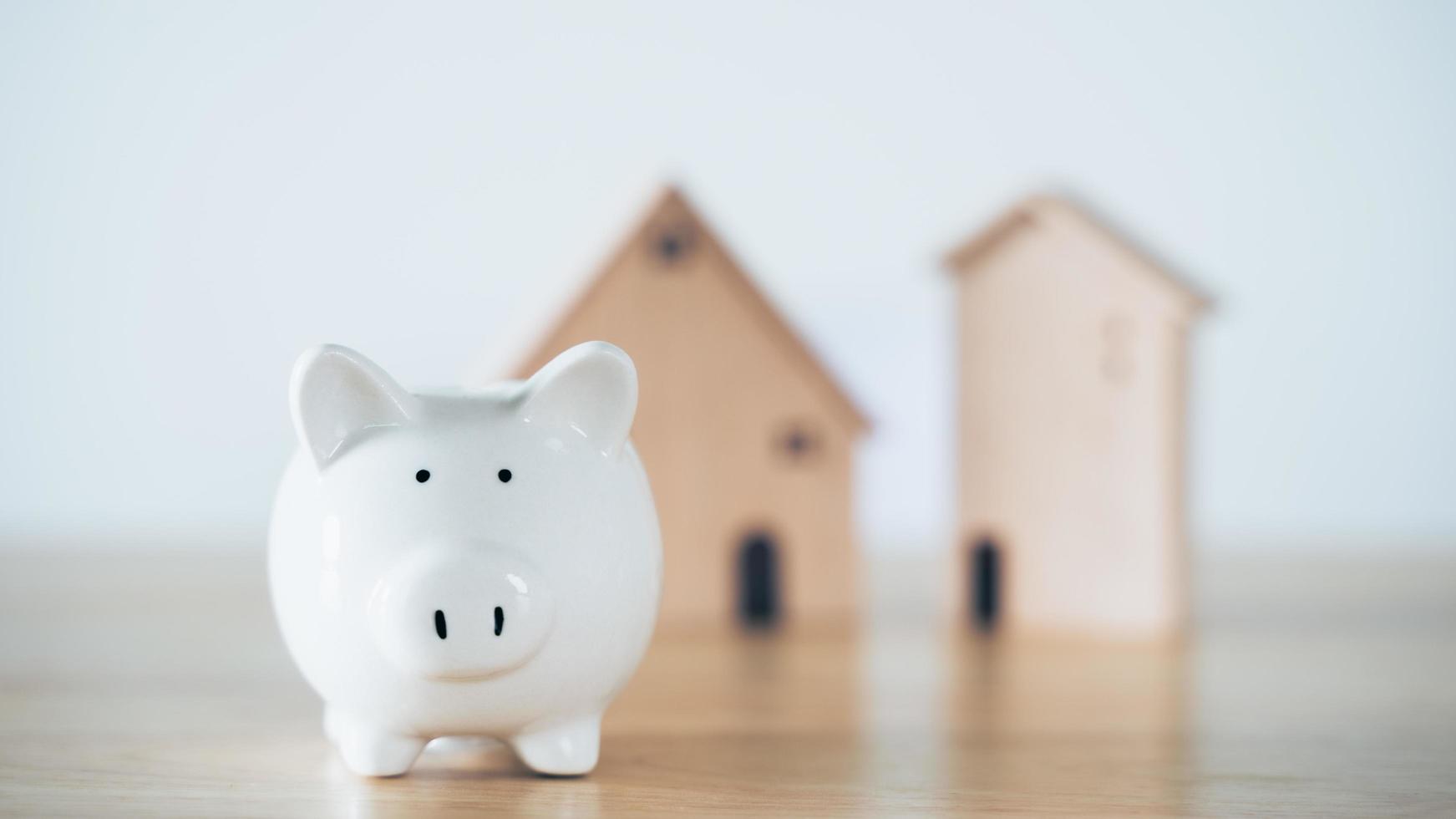 Wooden house with white piggy bank on wooden table. saving money for buying house, financial plan home loan concept. photo