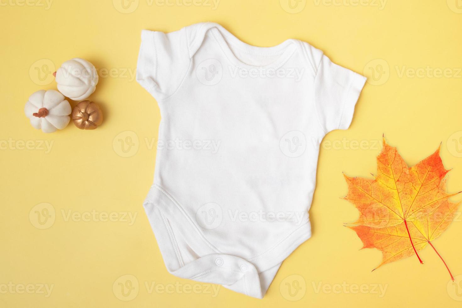 Vista superior de maqueta de traje de bebé con calabazas y hojas de arce sobre fondo amarillo para su texto o logotipo en la temporada de otoño foto