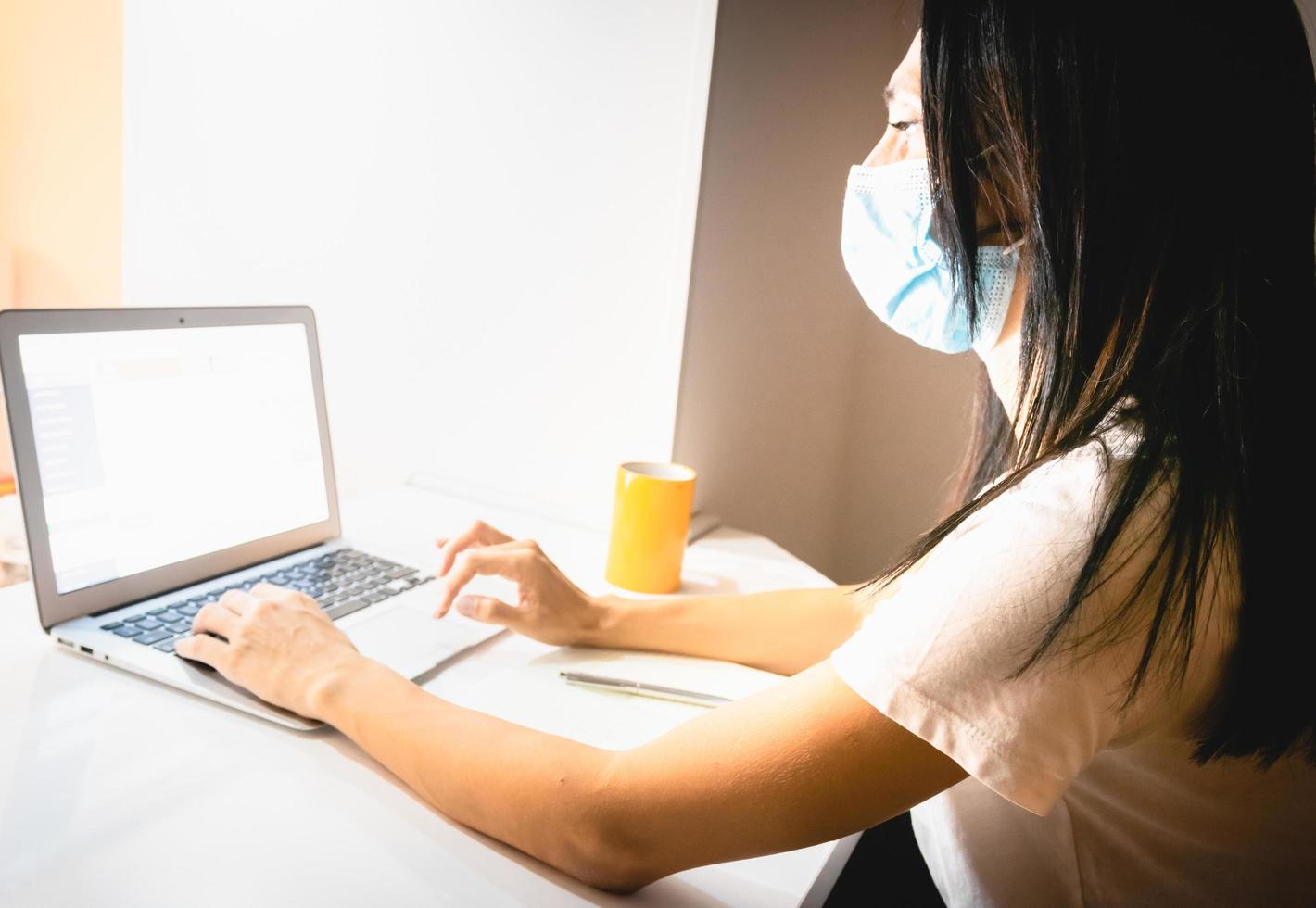 Young attractive caucasian woman is holding pen and writing notes in front of laptop in cozy room in the background. photo