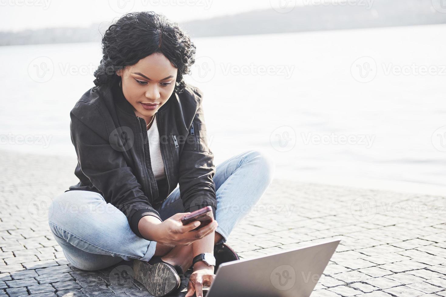 Mujer joven en la calle trabajando con un portátil y hablando por teléfono móvil foto