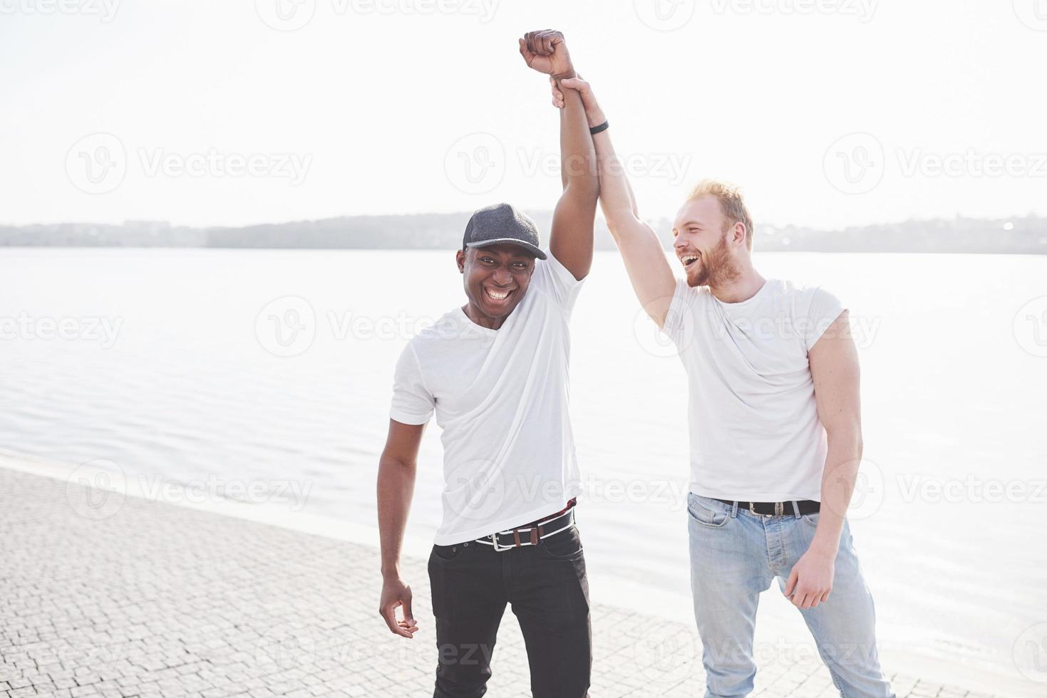 Dos jóvenes amigos multiétnicos hablando entre sí y sonriendo mientras foto