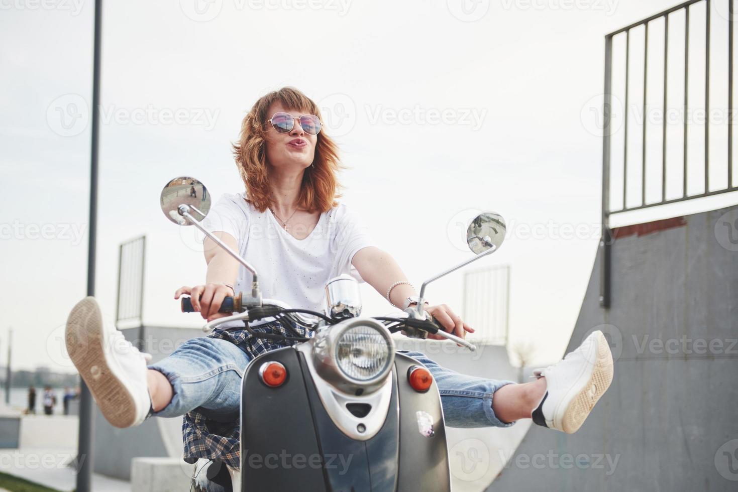 Portrait of a beautiful girl hipster sitting on a black retro scooter, smiling posing and enjoy the warm spring sunshine. photo