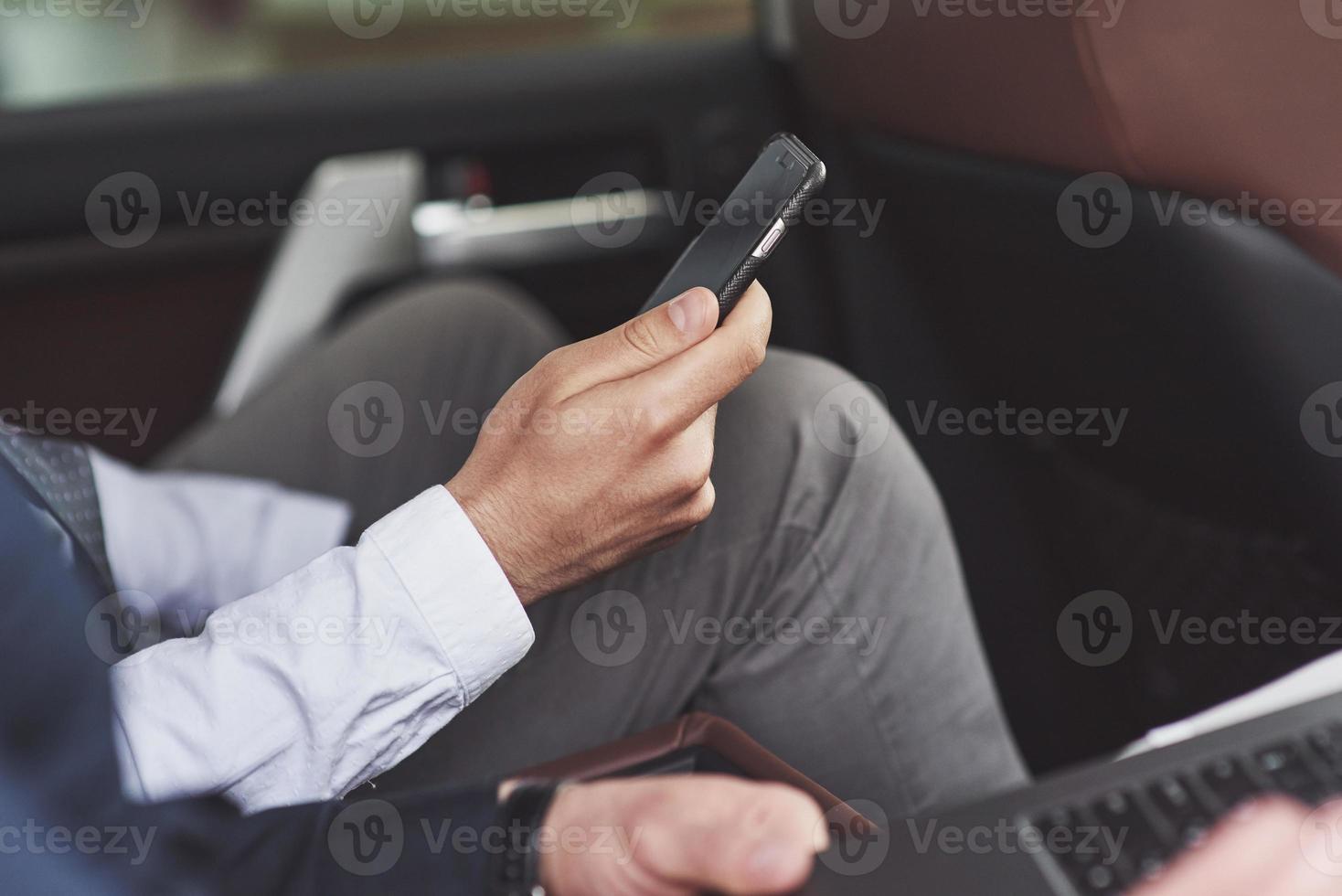 un empresario que envía un mensaje a un teléfono inteligente y se dirige al asiento trasero del automóvil. foto