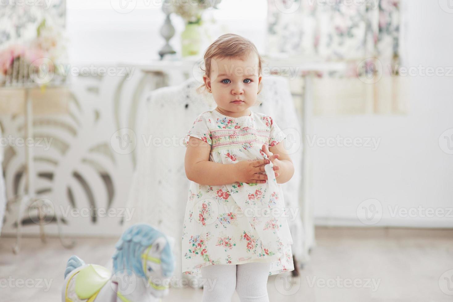 Childhood concept. baby girl in cute dress siting at bed playing with toys by the home. White vintage childroom photo