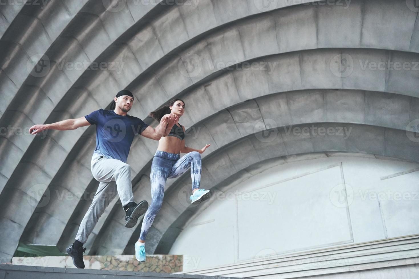 Young happy sports couple in the city street, performing parkour. photo