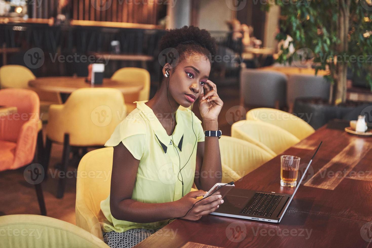 Joven y bella mujer de negocios afroamericana hablando por teléfono mientras trabajaba en un café foto