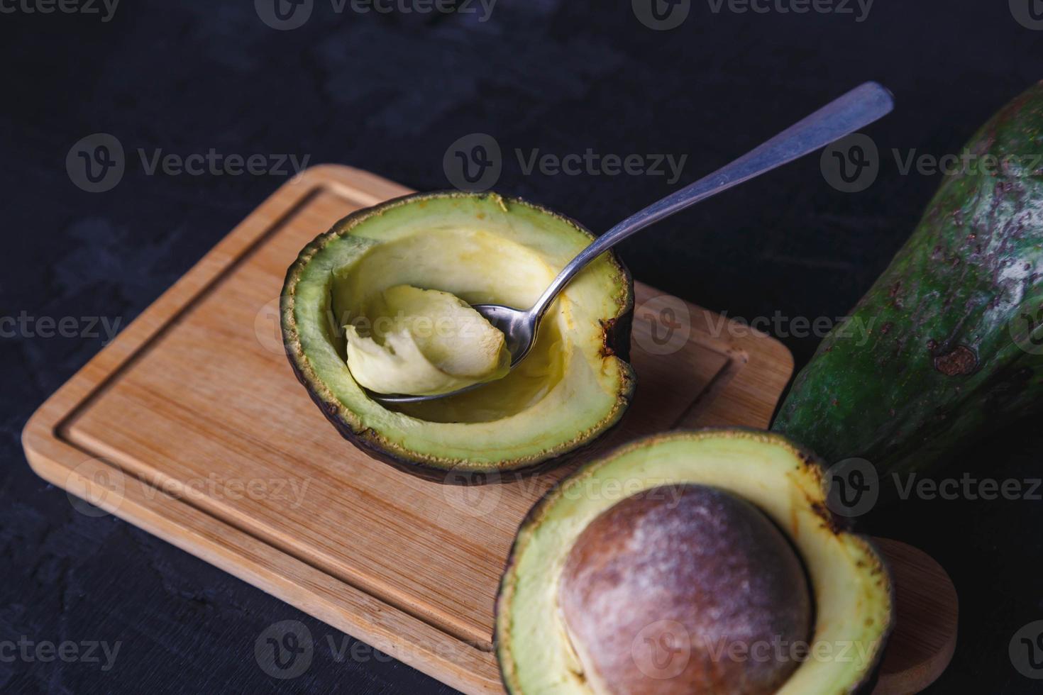 Fruta de aguacate cortado por la mitad sobre fondo de madera negra foto