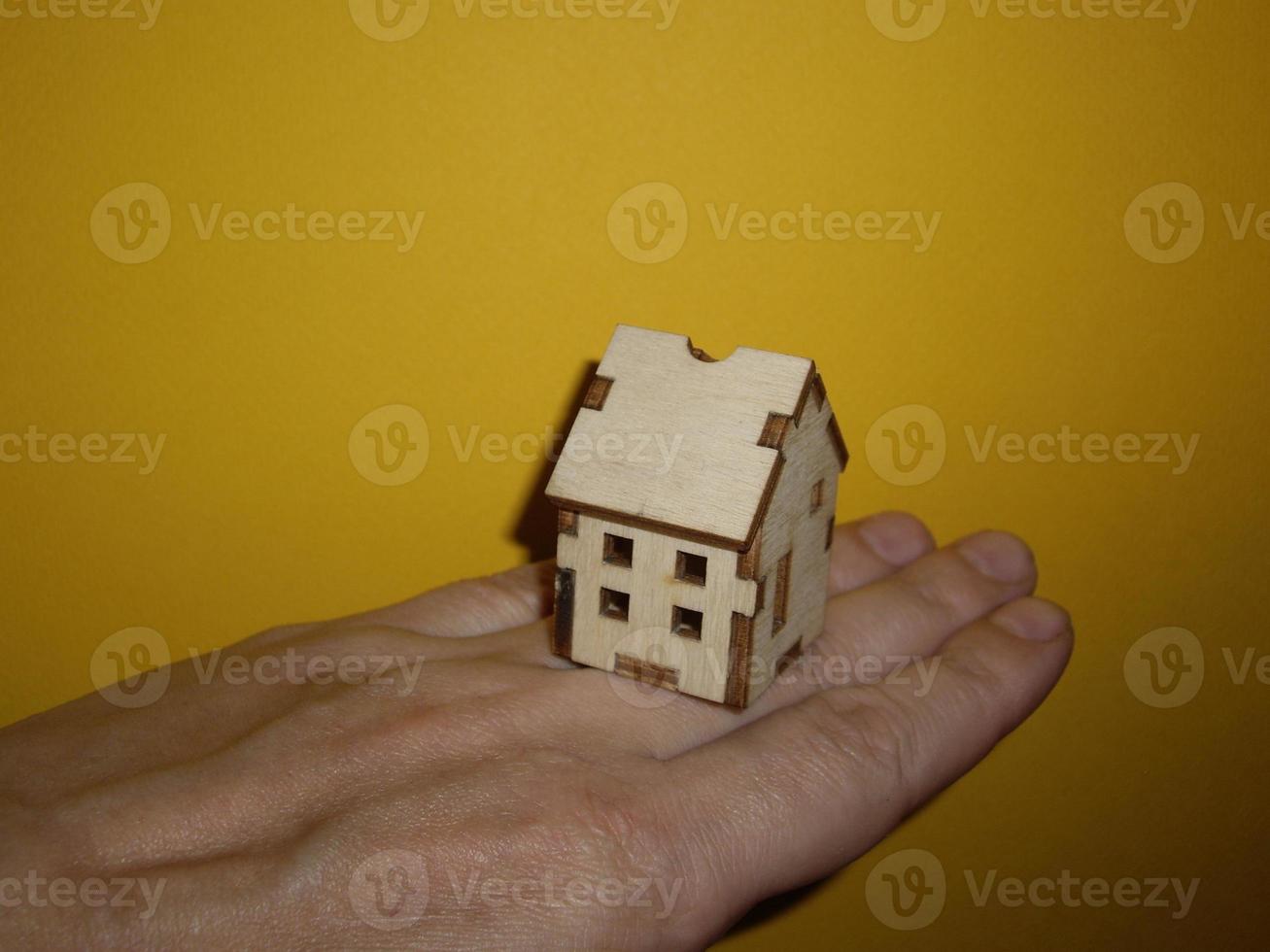 Pequeña casa de madera en la mano de un hombre sobre un fondo amarillo foto