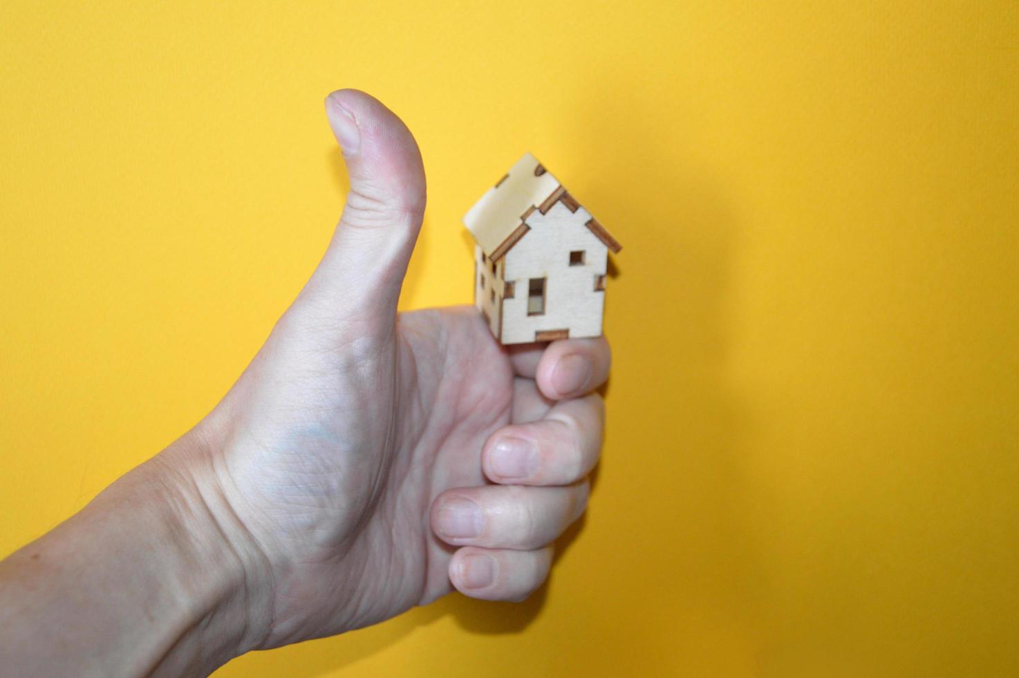 Small wooden house in a man's hand on a yellow background photo