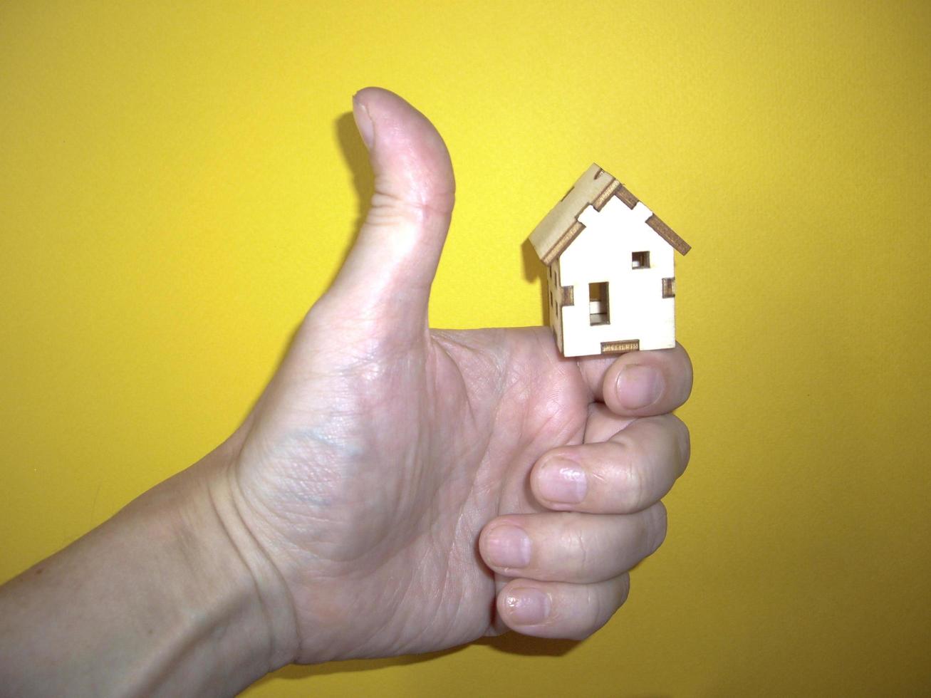 Small wooden house in a man's hand on a yellow background photo