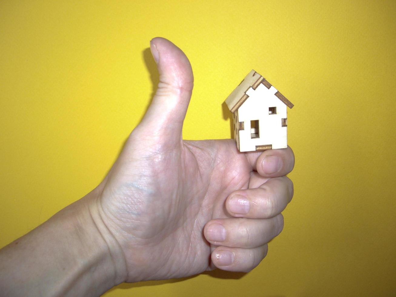 Pequeña casa de madera en la mano de un hombre sobre un fondo amarillo foto