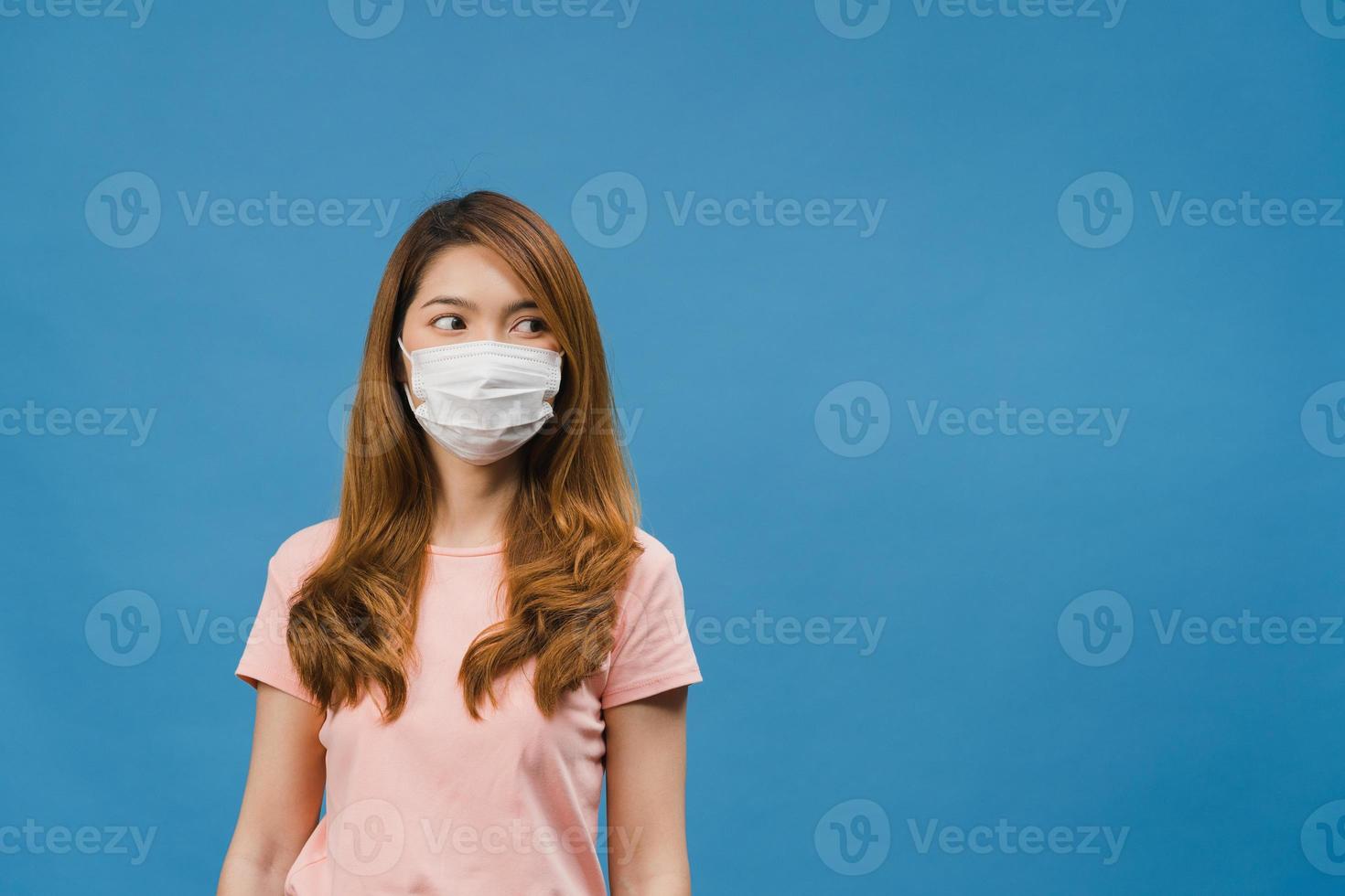 joven asiática con mascarilla médica vestida con ropa casual y mirando el espacio en blanco aislado sobre fondo azul. autoaislamiento, distanciamiento social, cuarentena para la prevención del virus corona foto