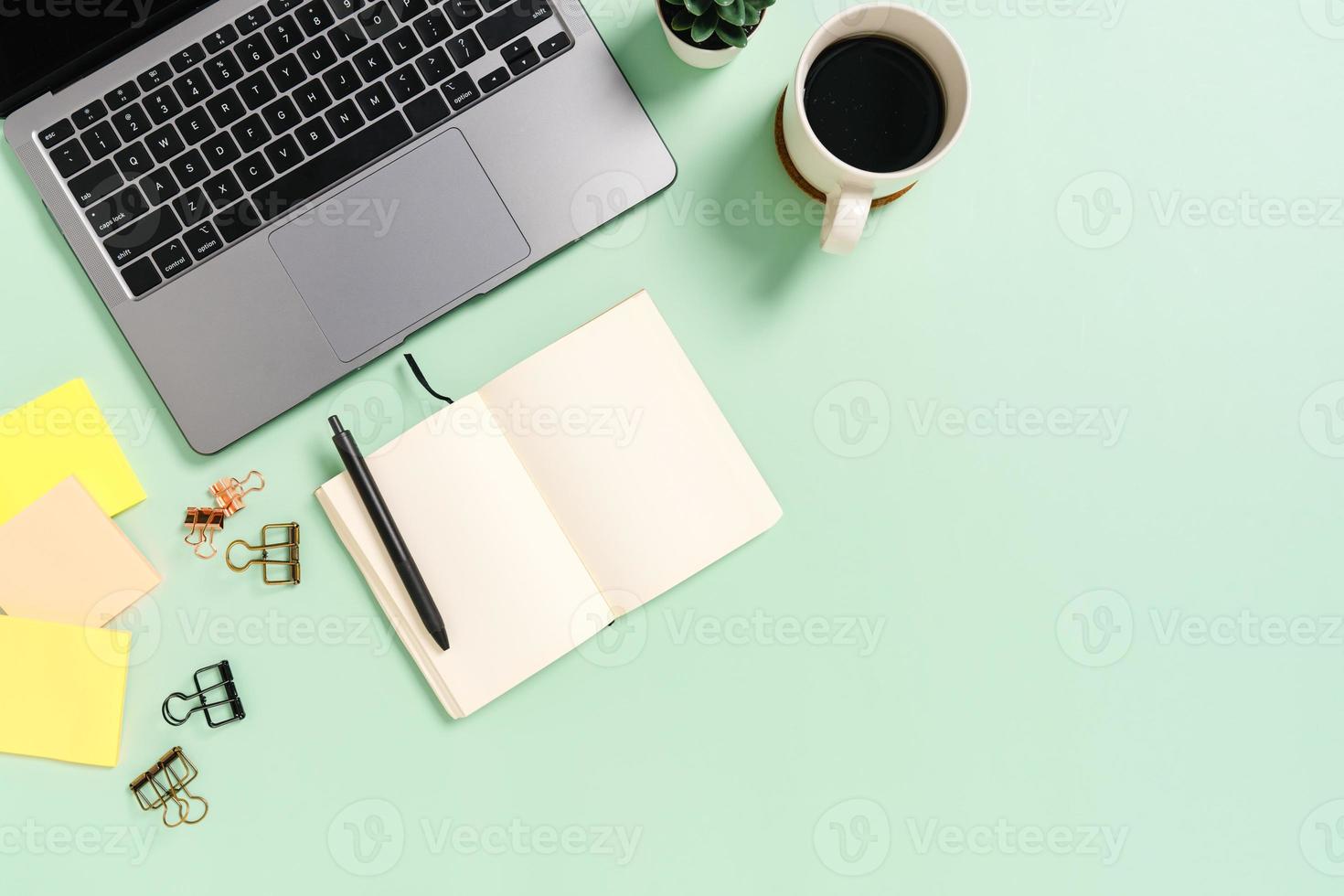 Creative flat lay photo of workspace desk. Top view office desk with laptop, coffee cup and open mockup black notebook on pastel green color background. Top view mock up with copy space photography.