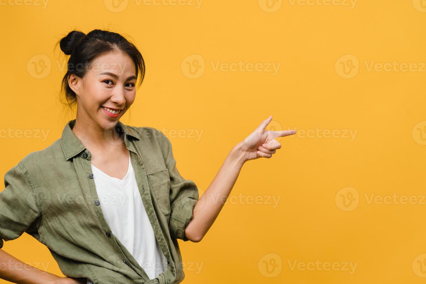 Retrato de joven asiática sonriendo con expresión alegre, muestra algo sorprendente en el espacio en blanco en un paño casual y mirando a cámara aislada sobre fondo amarillo. concepto de expresión facial. foto
