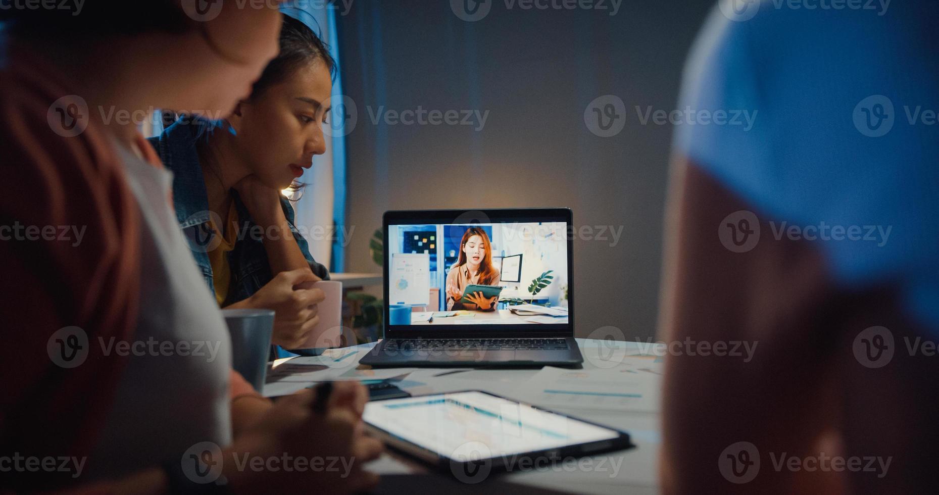 Asia businesswomen using laptop talk to colleagues about plan in video call meeting at home office. Working from house overload at night, remotely work, social distancing, quarantine for coronavirus. photo