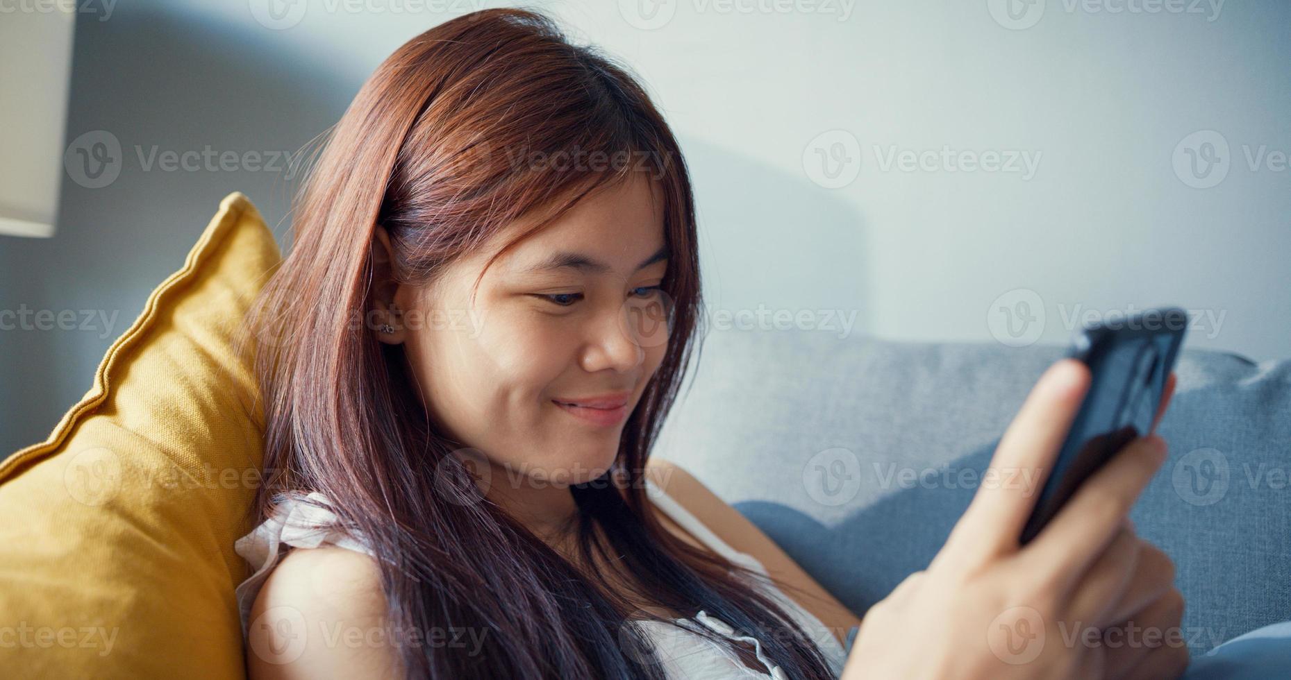 Happy youth Asia girl teenage with relax time use smartphone have fun gossip chat with college friends in living room at home. Isolate activity lifestyle, Social distance coronavirus pandemic concept. photo
