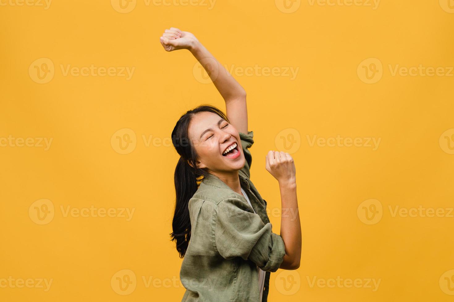 jovencita de asia con expresión positiva, alegre y emocionante, vestida con ropa casual sobre fondo amarillo con espacio vacío. feliz adorable mujer alegre se regocija con el éxito. concepto de expresión facial. foto