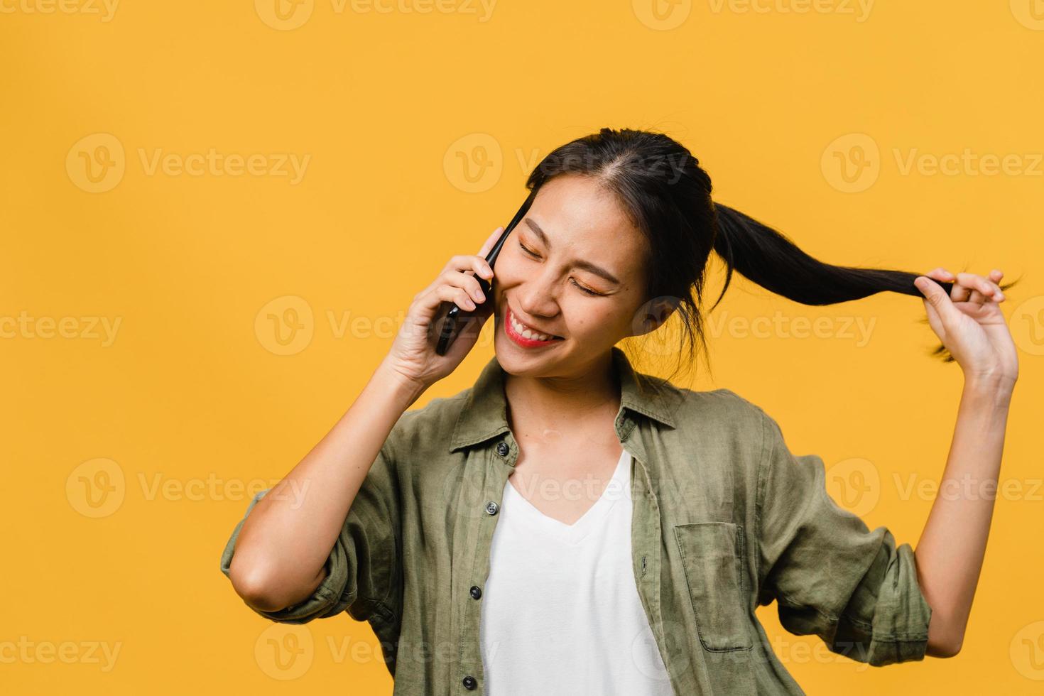 Jovencita asiática habla por teléfono con expresión positiva, sonríe ampliamente, vestida con ropa informal sintiendo felicidad y parada aislada sobre fondo amarillo. feliz adorable mujer alegre se regocija con el éxito. foto