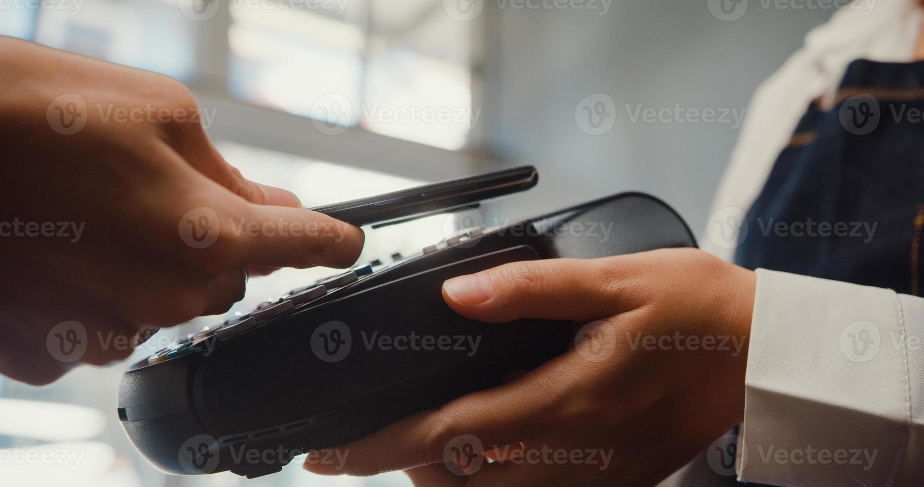 Joven mujer de Asia uso de autoservicio teléfono móvil pago sin contacto con máquina de lector de tarjetas de crédito en el café restaurante. propietario de una pequeña empresa, tecnología sin efectivo y concepto de transferencia de dinero. fotografía de cerca. foto