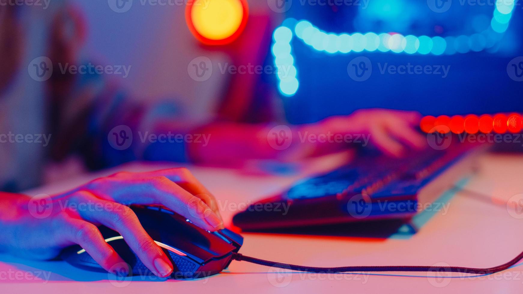 Close-up hands shot asia girl gamer use keyboard and mouse controller play video game with neon light computer in desk at home. Online esport streaming game online, Home quarantine activity concept. photo