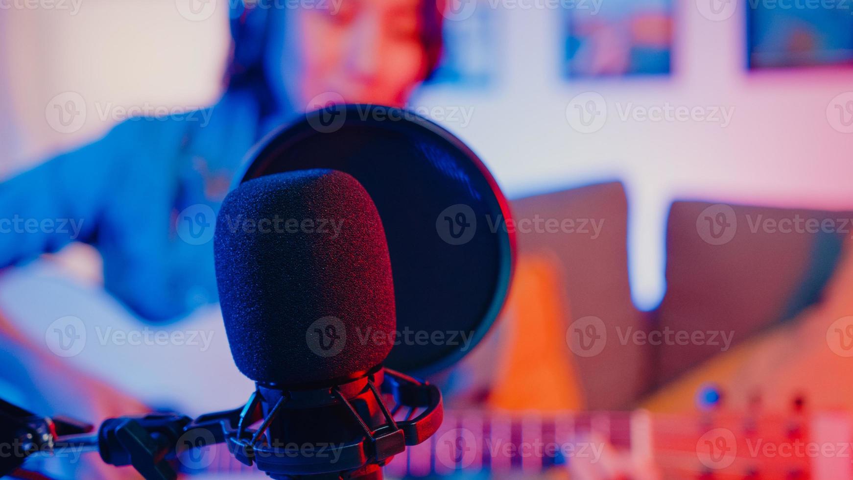 Happy asia girl blogger play guitar and use microphone sing song record music sound mixer on laptop in modern living room home studio at night. Music content creator, Tutorial, Broadcast concept. photo