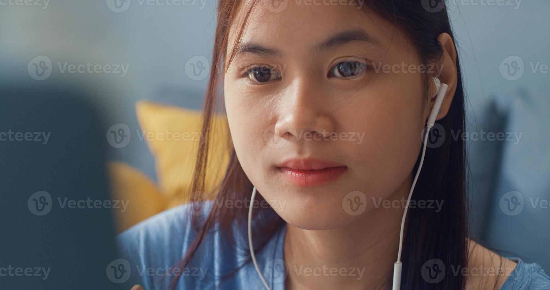 Young Asia girl teenager with casual wear headphones use laptop computer learn online write lecture notebook in living room at house. Isolate education online e-learning coronavirus pandemic concept. photo