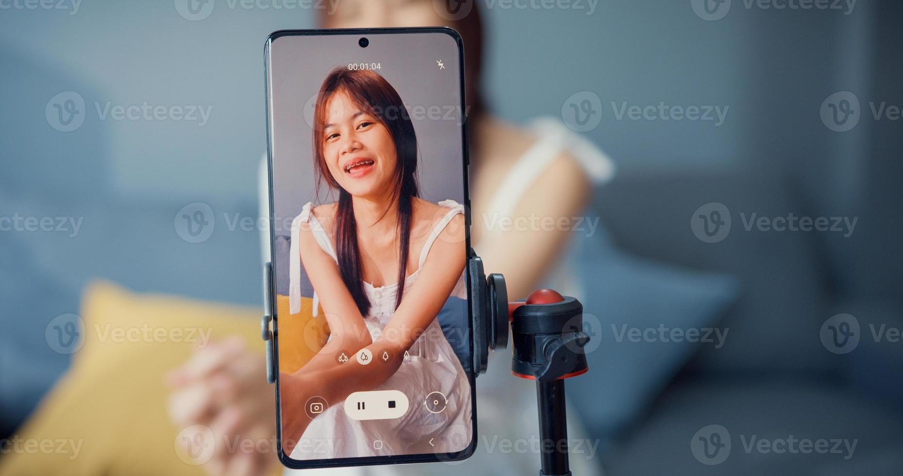 Happy young Asian girl blogger in front of phone camera use tablet enjoy question answer with follower in living room at home. Blogger activity lifestyle, Social distance coronavirus pandemic concept. photo