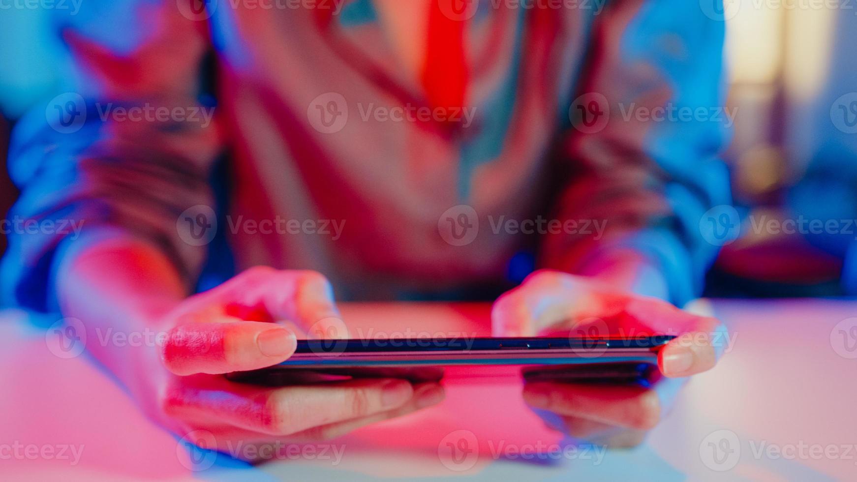 Close-up hands shot asia girl gamer use smartphone play online game colorful neon light on desk in living room at home. Online esport streaming game online, Home quarantine activity concept. photo