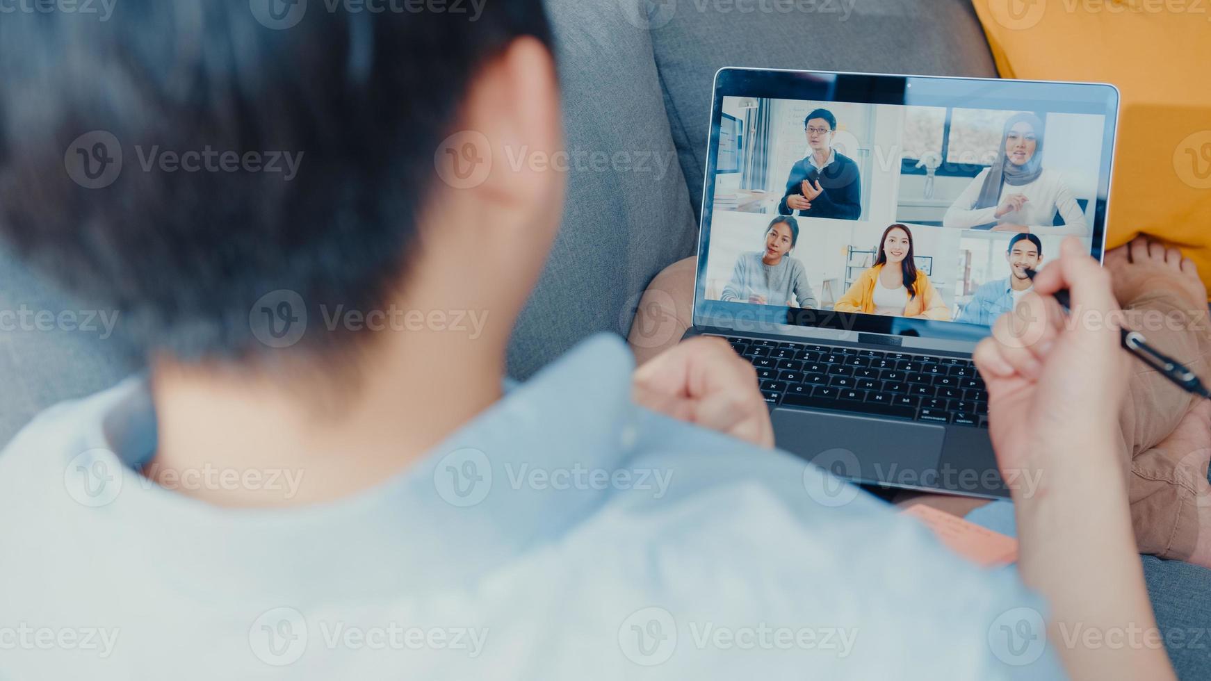 Young Asia businessman using laptop talk to colleagues about plan in video call meeting while work from home at living room. Self-isolation, social distancing, quarantine for corona virus prevention. photo