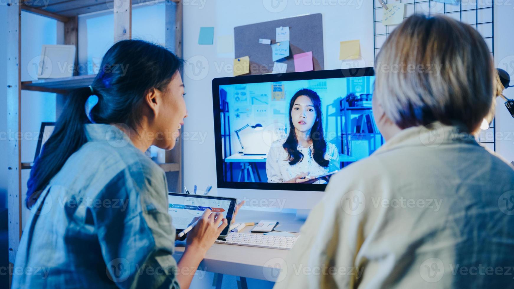 Mujeres empresarias asiáticas que usan el escritorio para hablar con sus colegas sobre el plan en una reunión de videollamada en la sala de estar. trabajando desde casa por sobrecarga nocturna, trabajo a distancia, distanciamiento social, cuarentena por coronavirus. foto