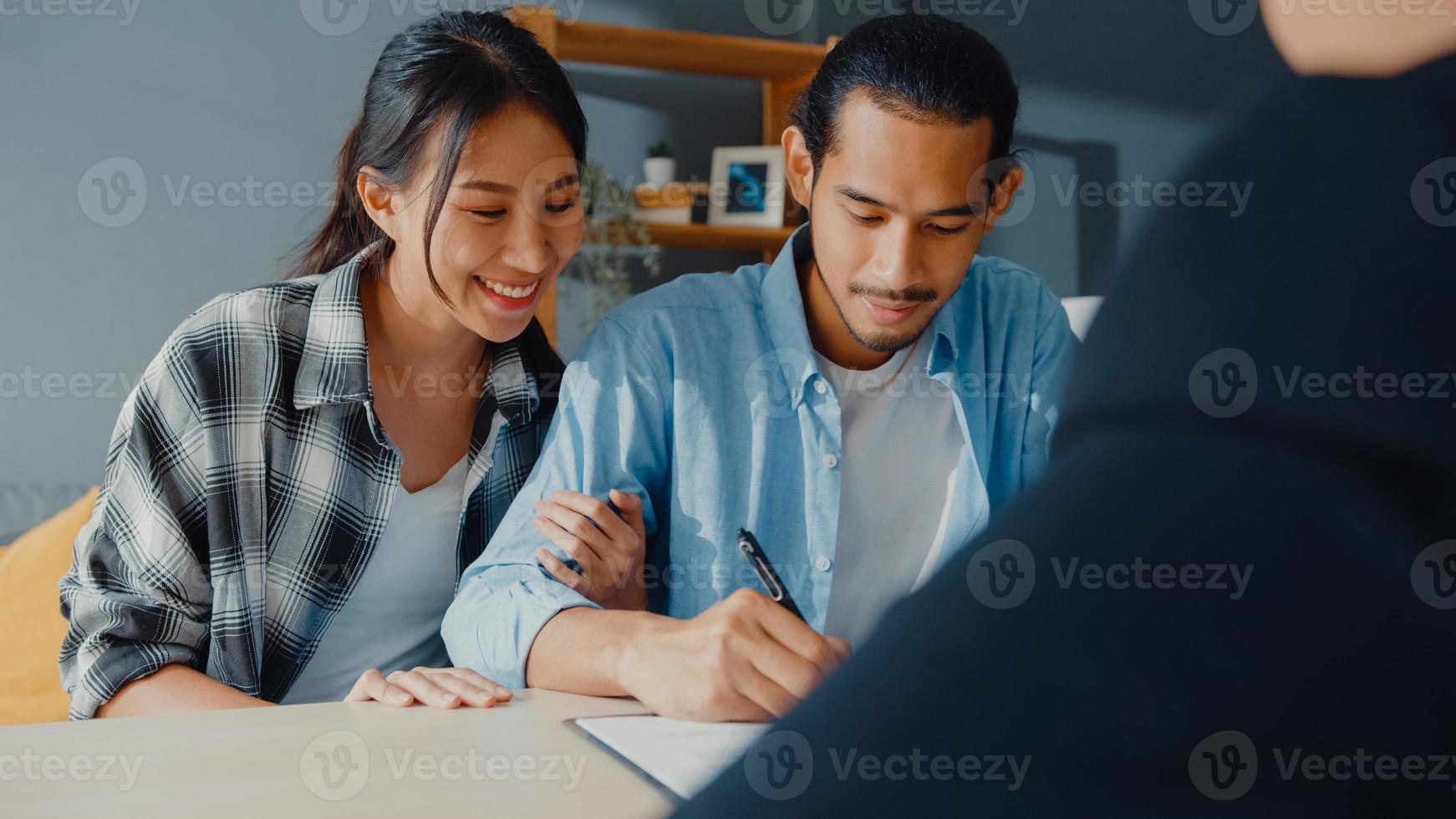 Happy asian young customer couple ready sign bank loan agreement for new house with broker agent, smiling husband and wife consider finance investment insurance contract together in front of broker. photo