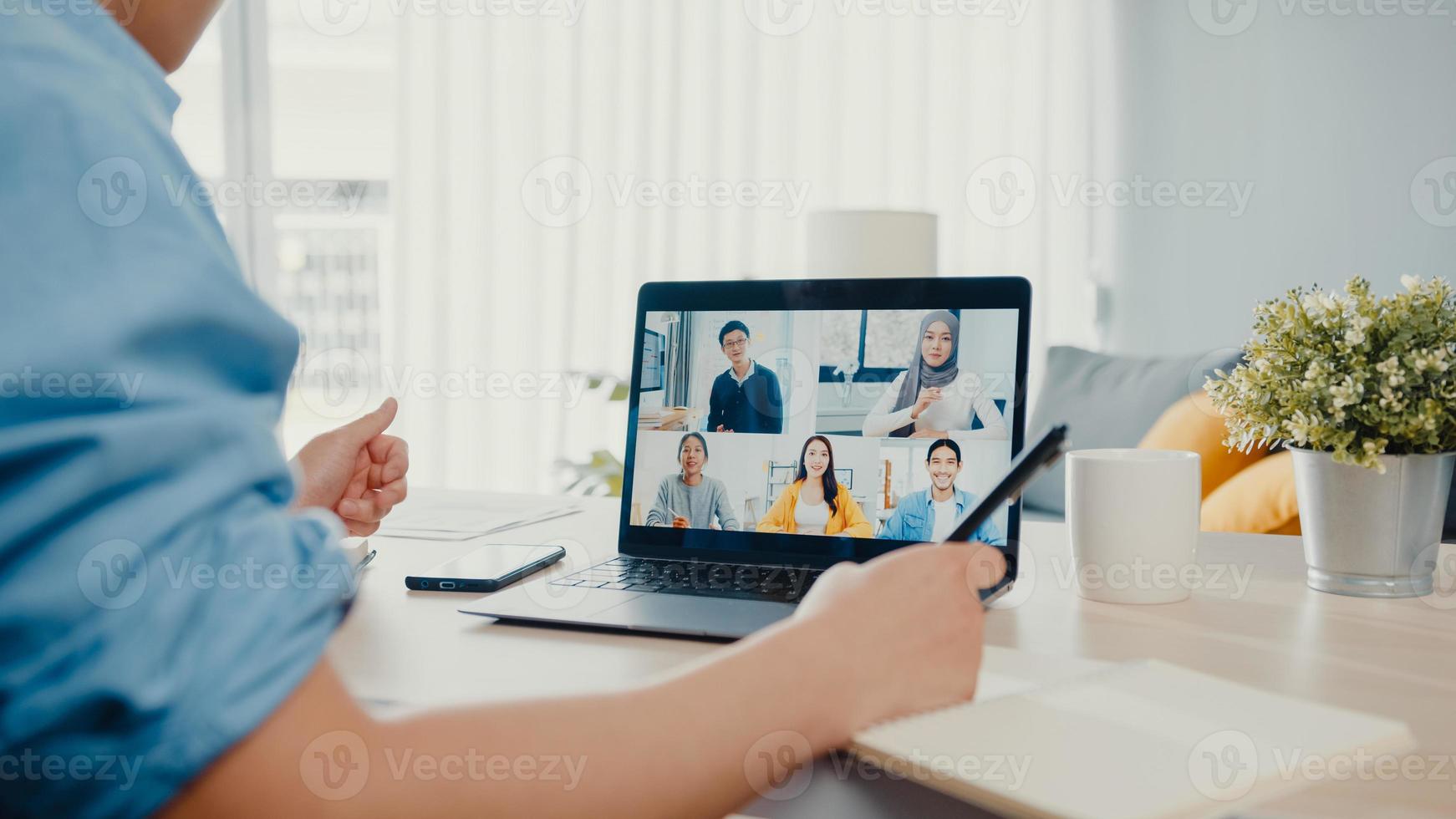 Young Asia businessman using laptop talk to colleagues about plan in video call meeting while work from home at living room. Self-isolation, social distancing, quarantine for corona virus prevention. photo