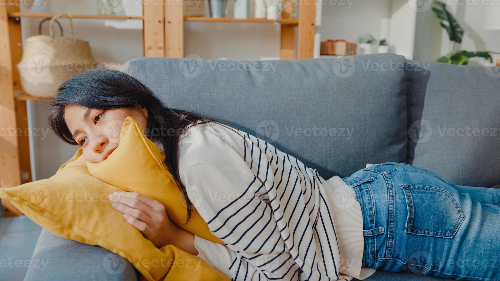 Joven mujer asiática se acuesta en un cómodo sofá en la sala de estar durmiendo después de un duro día de trabajo y se siente enferma y mal, la mujer cansada se queda dormida en el sofá en casa, toma una siesta o sueña despierta, concepto de fatiga. foto