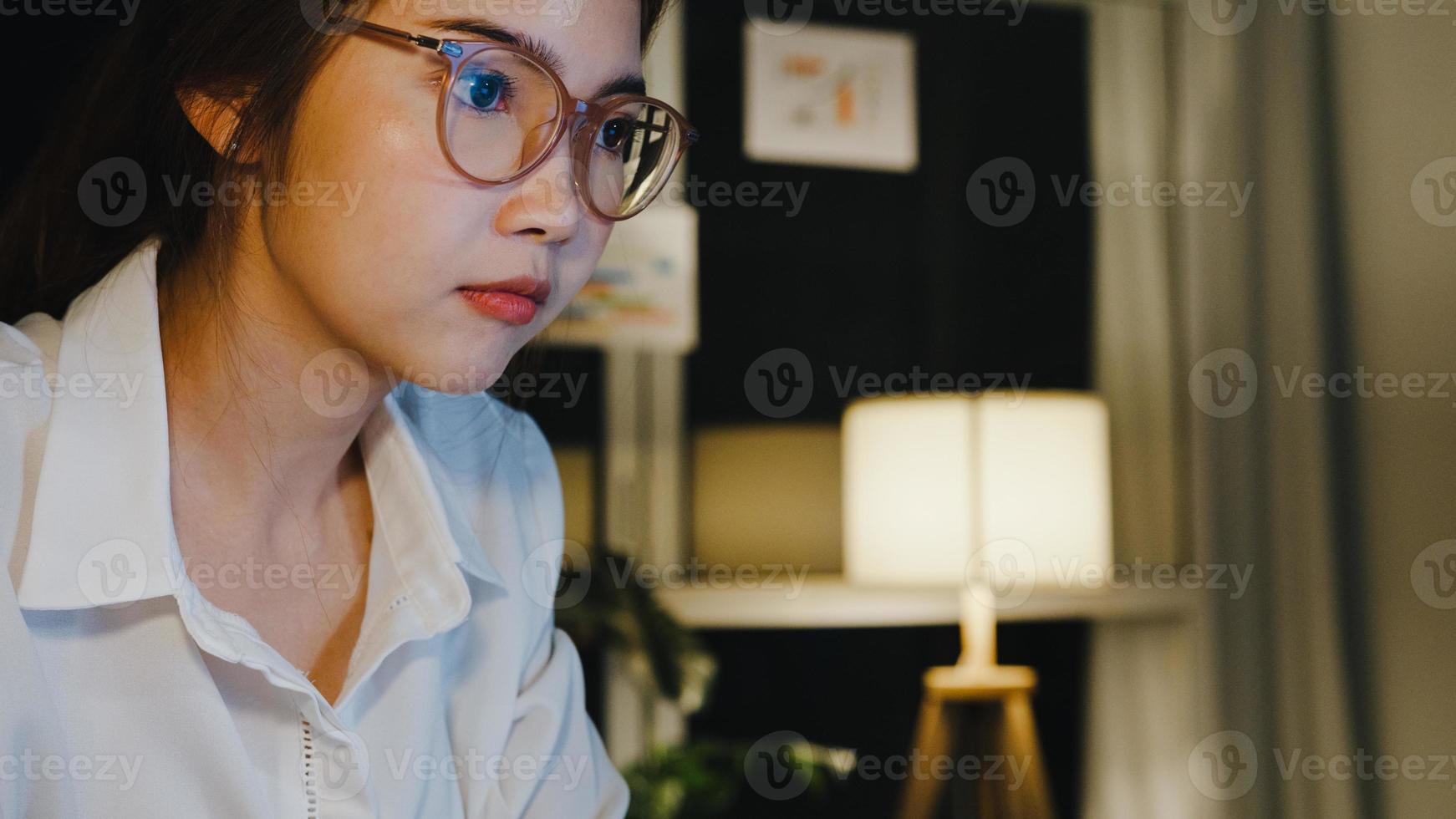 Freelance Asia lady using laptop hard work in living room at house. Working from home overload at night, remotely work, self isolation, social distancing, quarantine for corona virus prevention. photo