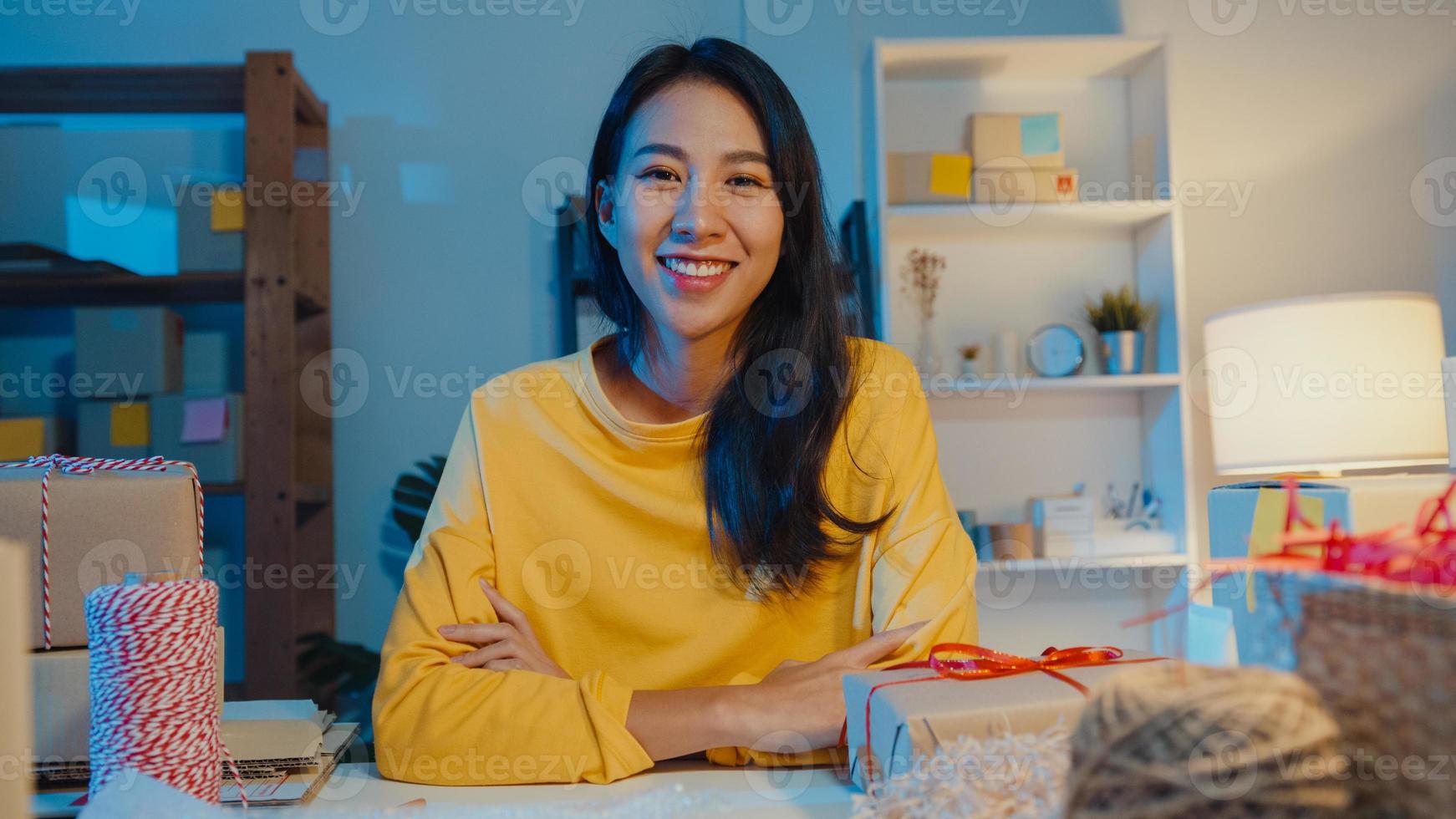 Portrait of young Asia businesswoman feeling happy smile, arms crossed and looking to camera while working store in home office at night. Small business owner, online market delivery concept. photo