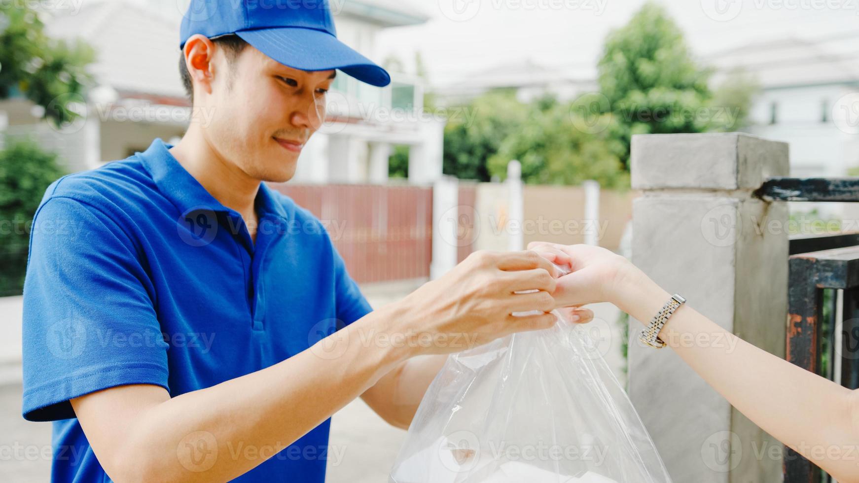 Young Asia postal delivery courier man in blue shirt handling food boxes for sending to customer at house and Asian female receive delivered package outdoors. Package shopping food delivery concept. photo