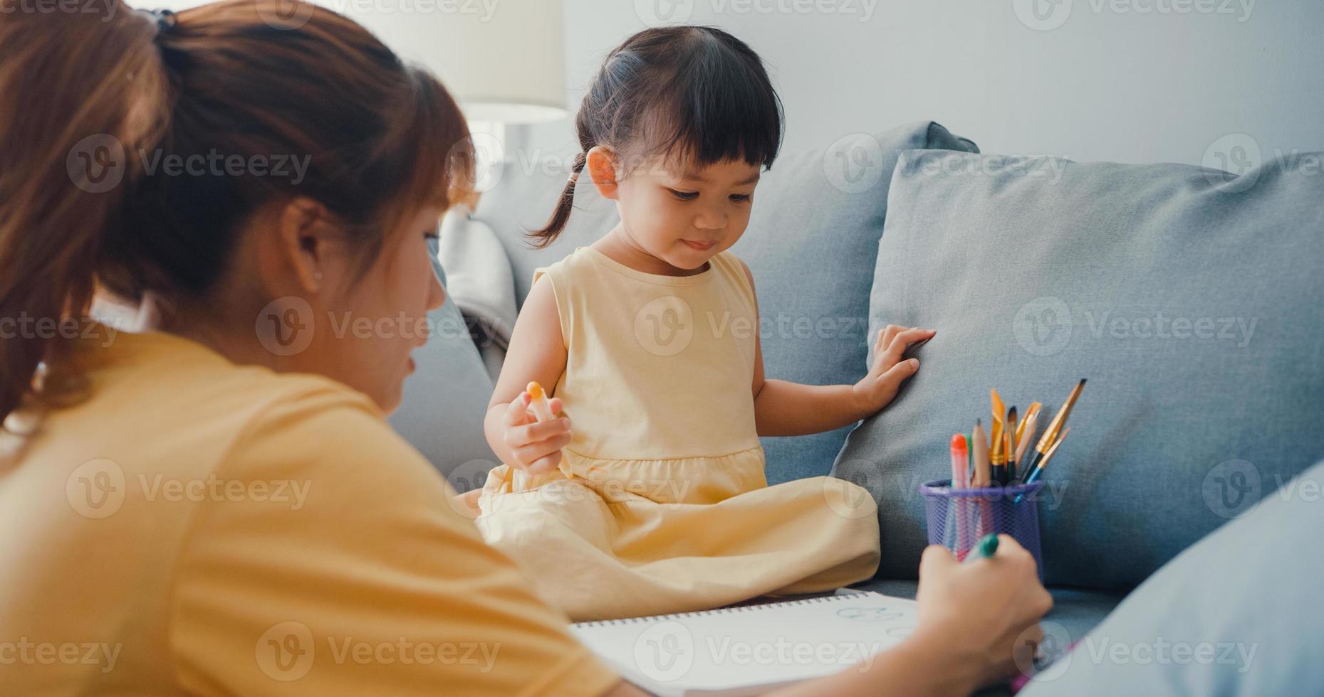 feliz, alegre, asia, familia, mamá, enseñar, niña, pintura, uso, álbum, y, colorido, lápices, divirtiéndose, relajarse, en, sofá, en, sala, en, casa. pasar tiempo juntos, distancia social, cuarentena por coronavirus. foto