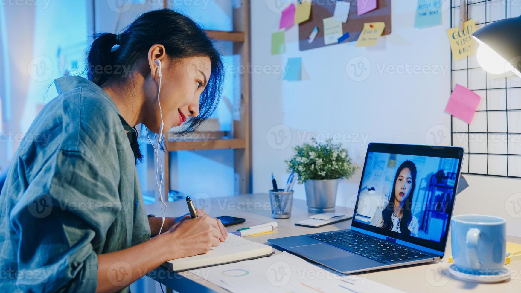 Asia empresaria usando laptop hablar con colegas sobre el plan en la reunión de videollamada en la sala de estar. trabajando desde casa por sobrecarga nocturna, trabajo a distancia, distanciamiento social, cuarentena por coronavirus. foto