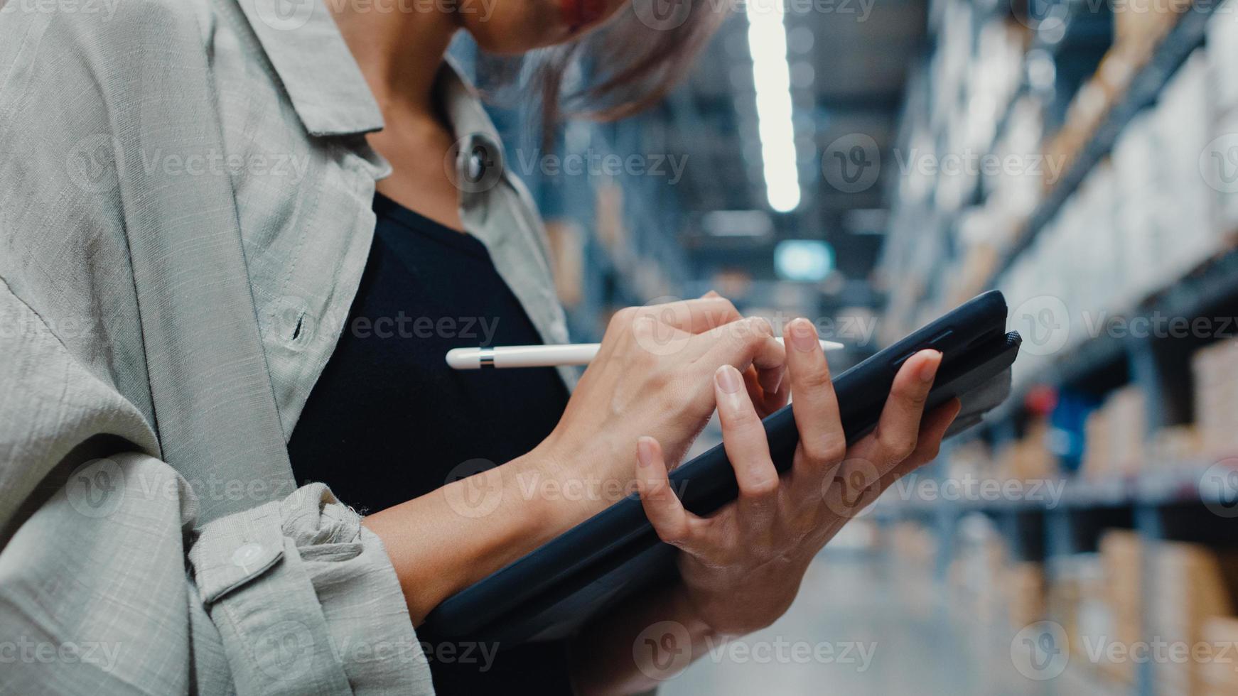 Attractive young Asia businesswoman manager looking for goods using digital tablet checking inventory levels standing in retail shopping center. Distribution, Logistics, Packages ready for shipment. photo