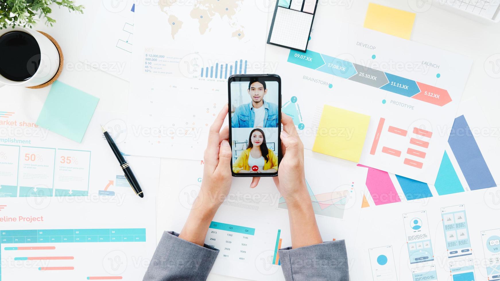 Top view of young Asia businesswoman using phone talk to colleague about plan in video call meeting while work from home at living room. Social distancing, quarantine for corona virus prevention. photo