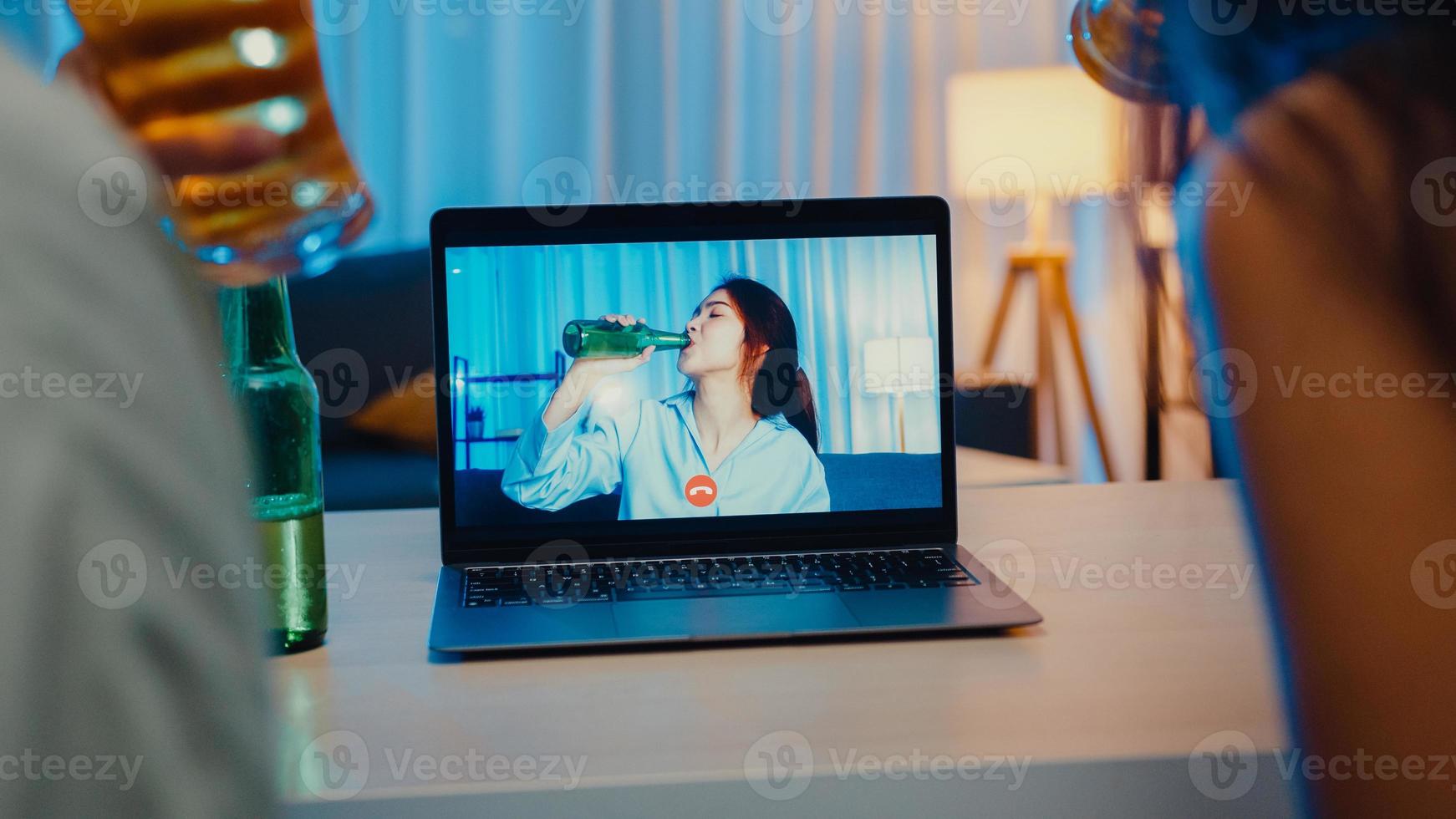 Joven mujer asiática bebiendo cerveza divirtiéndose feliz momento fiesta nocturna evento celebración en línea a través de videollamada en la sala de estar de la casa por la noche. distanciamiento social, cuarentena para la prevención del coronavirus. foto